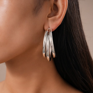 Close-up of a model wearing layered silver geometric C-shaped metal hoop earrings