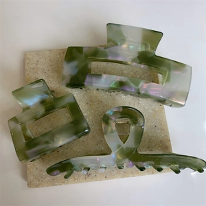 Detail of green and white marbled acetate hair claws with pearlescent finish on a coaster