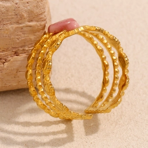 Detail eines mehrlagigen 18K vergoldeten Wellenrings mit rosa Stein auf Steinfläche