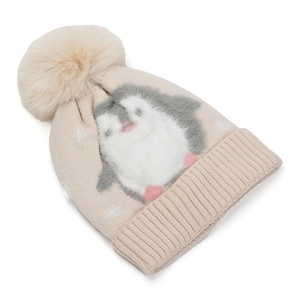 Detail of beige knit hat with penguin pattern and fluffy pom-pom for winter warmth