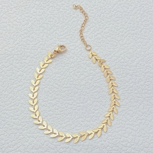 Bohemian 18K gold arrow leaf anklet chain for women on a textured white surface