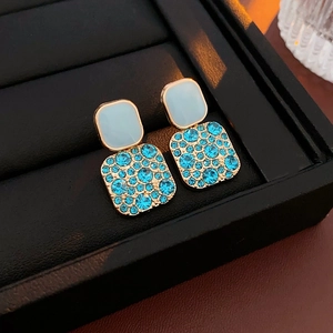Elegant gold square earrings with light blue stones and pavé set blue crystals on a display