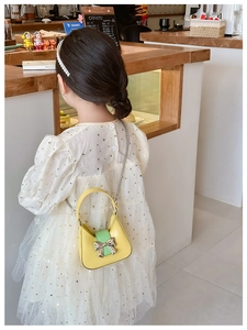 Detail of child wearing yellow PU crossbody bag with silver bow and chain strap