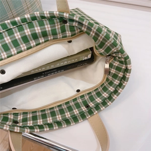 Interior detail of green plaid canvas tote showing leather straps and magnetic closure