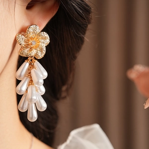 Détail de boucles d'oreilles fleuries à pompons avec perles portées par un modèle
