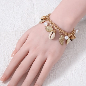Gold baroque shell and pearl charm bracelet displayed on a model wrist over a white background