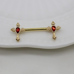 Detailed view of gold cross nipple rings featuring vibrant red drop-shaped gemstones