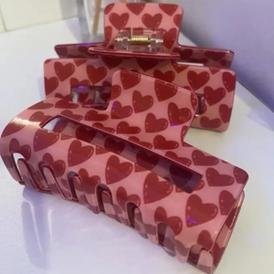 Détail de deux pinces à cheveux roses avec motifs de cœurs rouges sur fond blanc pur