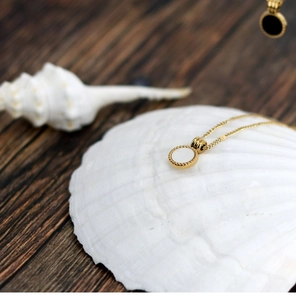 Detailed macro view of an 18K gold-plated circular white shell pendant on a wood surface