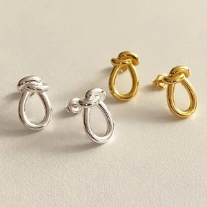 Detailed view of polished gold and silver knot-style drop earrings on a light surface