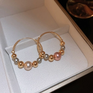 Detailed close-up of gold twist hoop earrings with gradient grey and champagne pearls