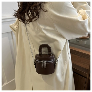 Vue arrière du modèle portant un sac cylindrique en cuir marron à chaîne argentée