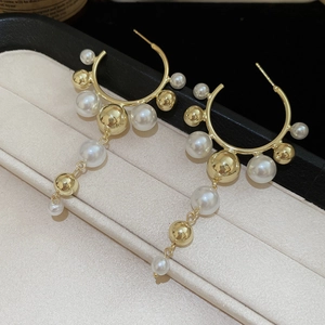 Detail of C-shaped pearl drop earrings with gold beads in a beige jewelry gift box