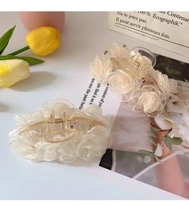 Detailed view of beige organza flower hair claws with elegant metal tassels on white surface