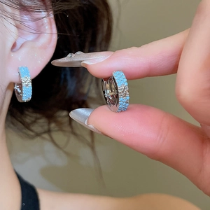 Detail of silver hoop earring with blue beads and a gold cross star motif on ear