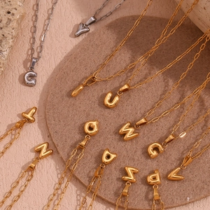 Close-up of 18K gold and silver mini bubble letter pendants on paperclip chain necklaces