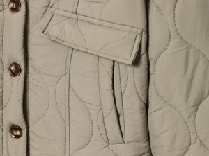 Detail of wave-quilted jacket with dark tortoiseshell button and sage green fabric texture