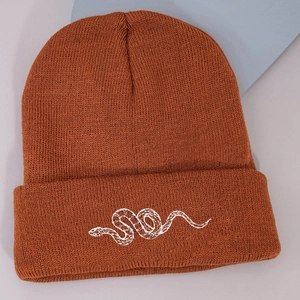 Detailed close-up of brown knit beanie featuring white snake embroidery and ribbed texture