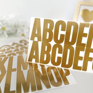 Detail of 2.5 inch gold metallic alphabet stickers on a decorative white background