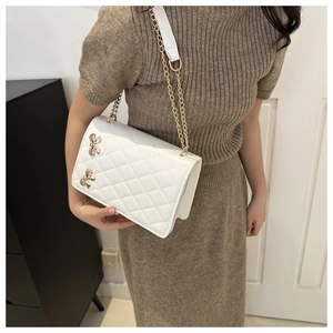 Close-up of white quilted crossbody bag featuring golden butterfly charms and chain strap