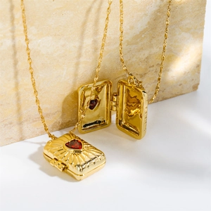 Detailed close-up of golden heart locket necklace with an inlaid red gemstone
