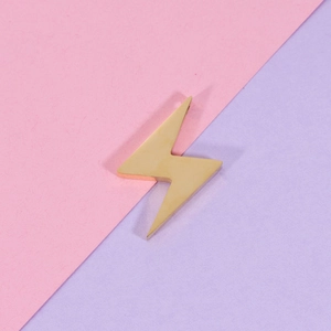 Macro detail of lightning bolt shaped golden stainless steel pendant on pastel background