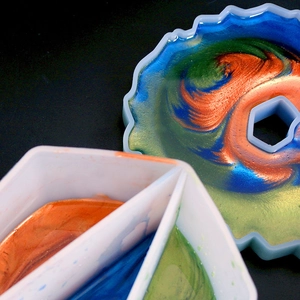 Macro view of silicone mold and mixing cup showing metallic resin fluid textures
