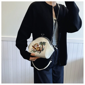 Detail of white shell bag featuring sloth embroidery and elegant black metal chain strap