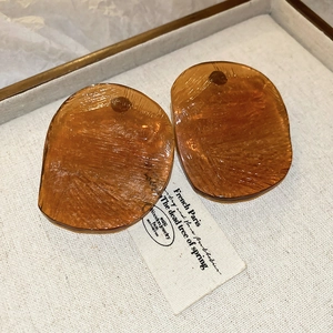 Macro shot of irregular amber resin earrings with brushed texture on linen display