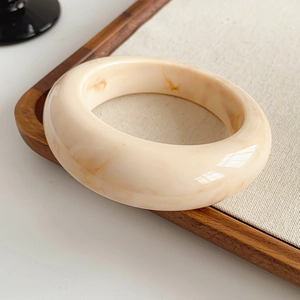 Close-up of a wide marble-patterned cream resin bangle on a wooden tray