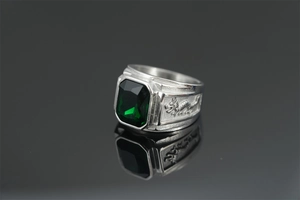 Macro detail of silver dragon ring featuring a rectangular green gemstone on black glass