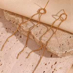 Close-up of golden long tassel drop earrings with snake chain on champagne silk fabric