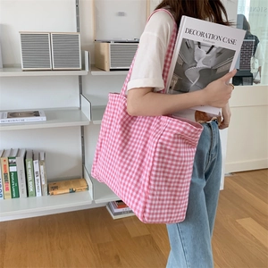 Detail view of pink checkered canvas tote bag worn by a model in a minimalist studio setting