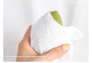 Detail of squeezing a green makeup sponge with a cotton towel to dry excess water