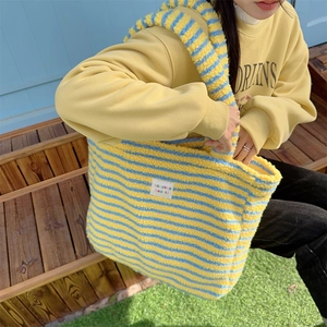 Detailed view of yellow and blue striped plush tote bag shown on outdoor wooden steps
