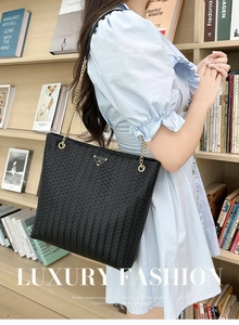 Close-up of black woven tote bag with gold chain strap in a literary library setting