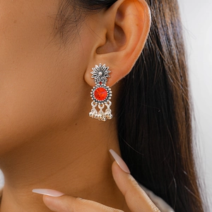Detailed close-up of retro silver flower earrings with red gemstone and small bell tassels
