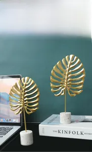 Detail of modern gold monstera leaf sculptures with white marble terrazzo cylinder bases