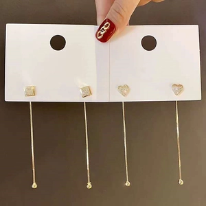 Détail de boucles d'oreilles dorées à pampilles avec strass carrés et en cœur