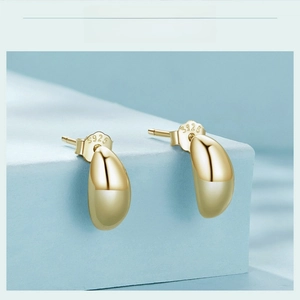 Macro shot of polished S925 sterling silver gold bean studs showing the metal hallmark