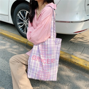 Detail of checkered canvas tote bag with pink grocery text used in daily commute