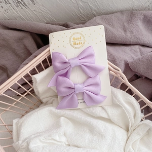 Détail de deux pinces à cheveux avec nœuds en tissu violet sur carte cadeau