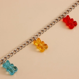 Detail of silver metal chain with red, yellow, and blue resin bear charms on beige background