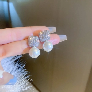 Close-up of elegant square diamond and pearl drop earrings held by hand