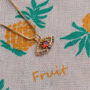 Macro shot of gold-plated evil eye pendant with red zircon and colorful small stones