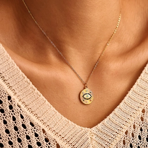 Collier œil maléfique doré avec pierres colorées porté par un mannequin sur un pull beige