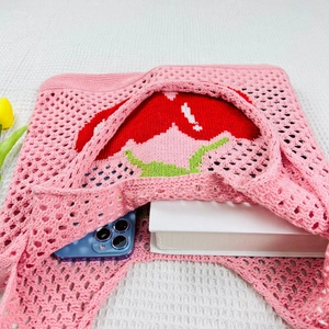 Pink knit tote bag detail with hollow pattern, blue smartphone, book and tulip accents