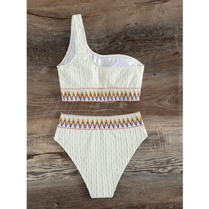 White one-shoulder high-waisted bikini set with colorful ethnic chevron trim on wood background