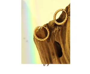 Macro shot of 18K gold plated hoop earrings with textured finish on wood background