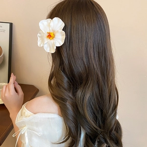 Close-up of a white hibiscus hair clip with yellow pistil worn on wavy brown hair
